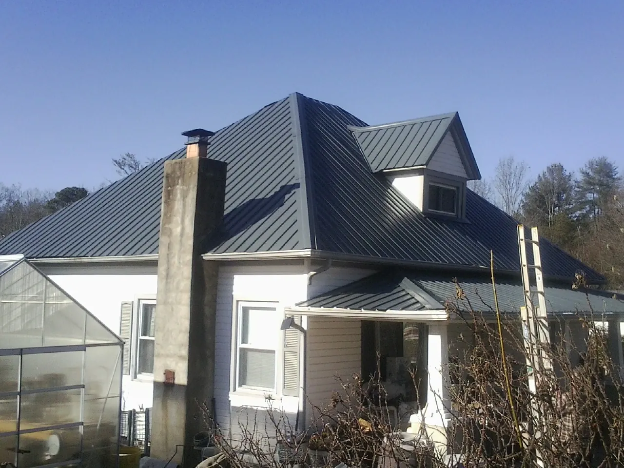 Dark blue standing seam metal roof on a white farmhouse with dormer — Slate & Tile Roof Repair by Roofing Brothers in Land O Lakes