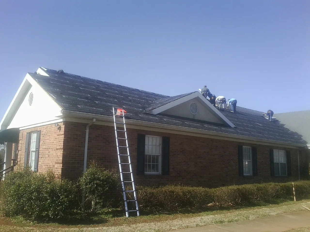 Crew tearing shingles off a brick ranch roof with a ladder set — Metal Roof Repair work by our crew in Land O Lakes