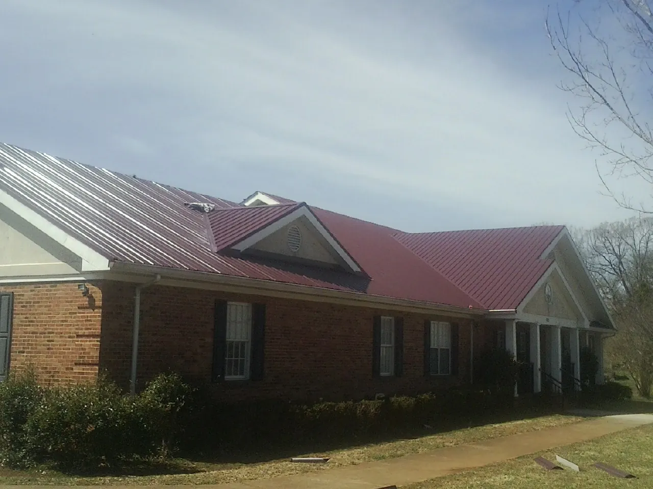 Red metal roof with gabled entries on a long brick building, from a Hail Damage Roof Repair job in Land O Lakes