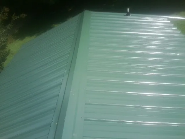 New green metal panels meeting at the ridge of a roof — Flat Roof Repair work by our crew in Land O Lakes