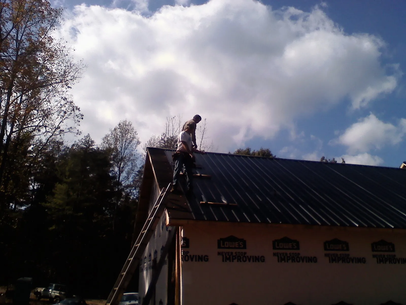 Roofer fastening dark metal panels high against a cloudy sky, from a Roof Inspection job in Land O Lakes