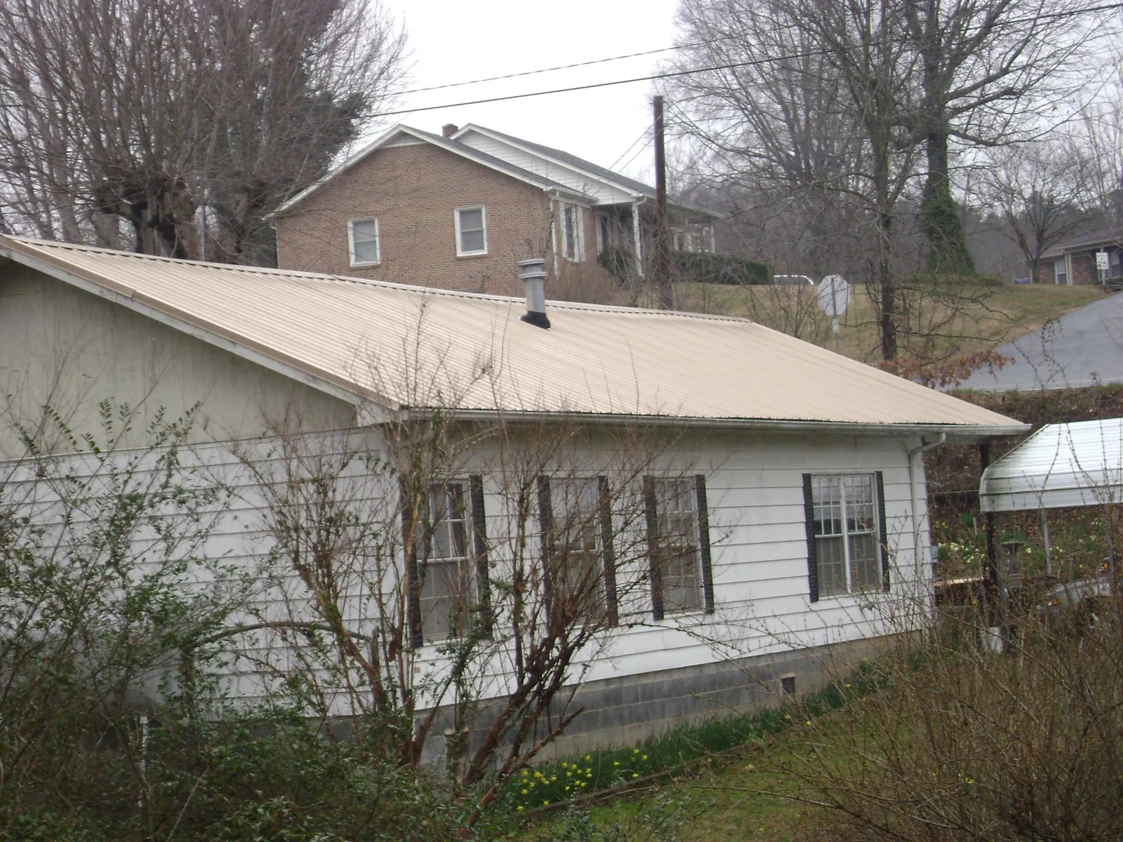 Tan metal roof on a white sided house set into a hillside — Commercial Roofing by Roofing Brothers in Land O Lakes