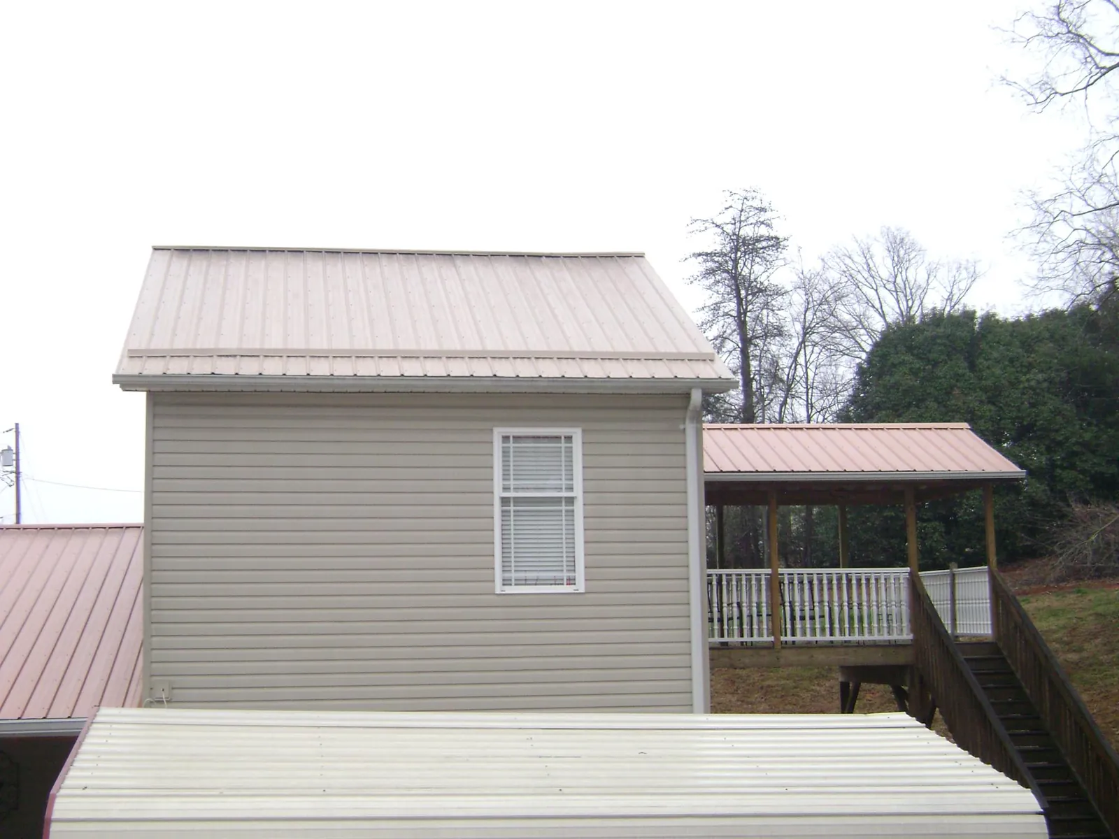 Tan metal roofs on a two story addition and attached porch, from a Roof Replacement job in Land O Lakes